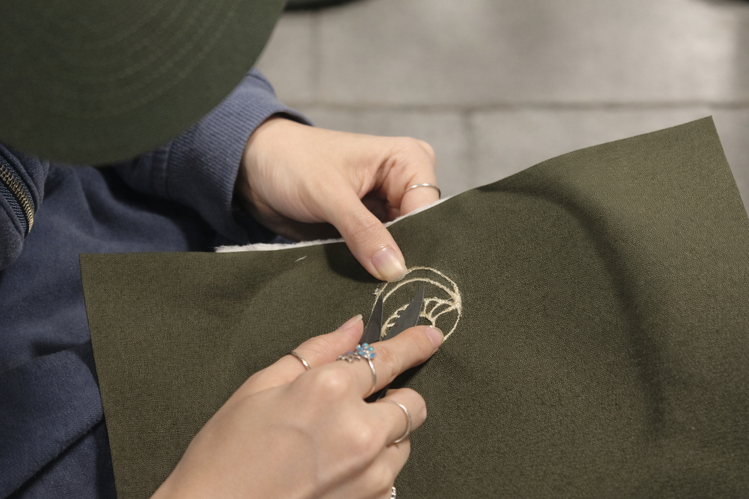 Person holding a piece of dark green fabric with a logo on it.