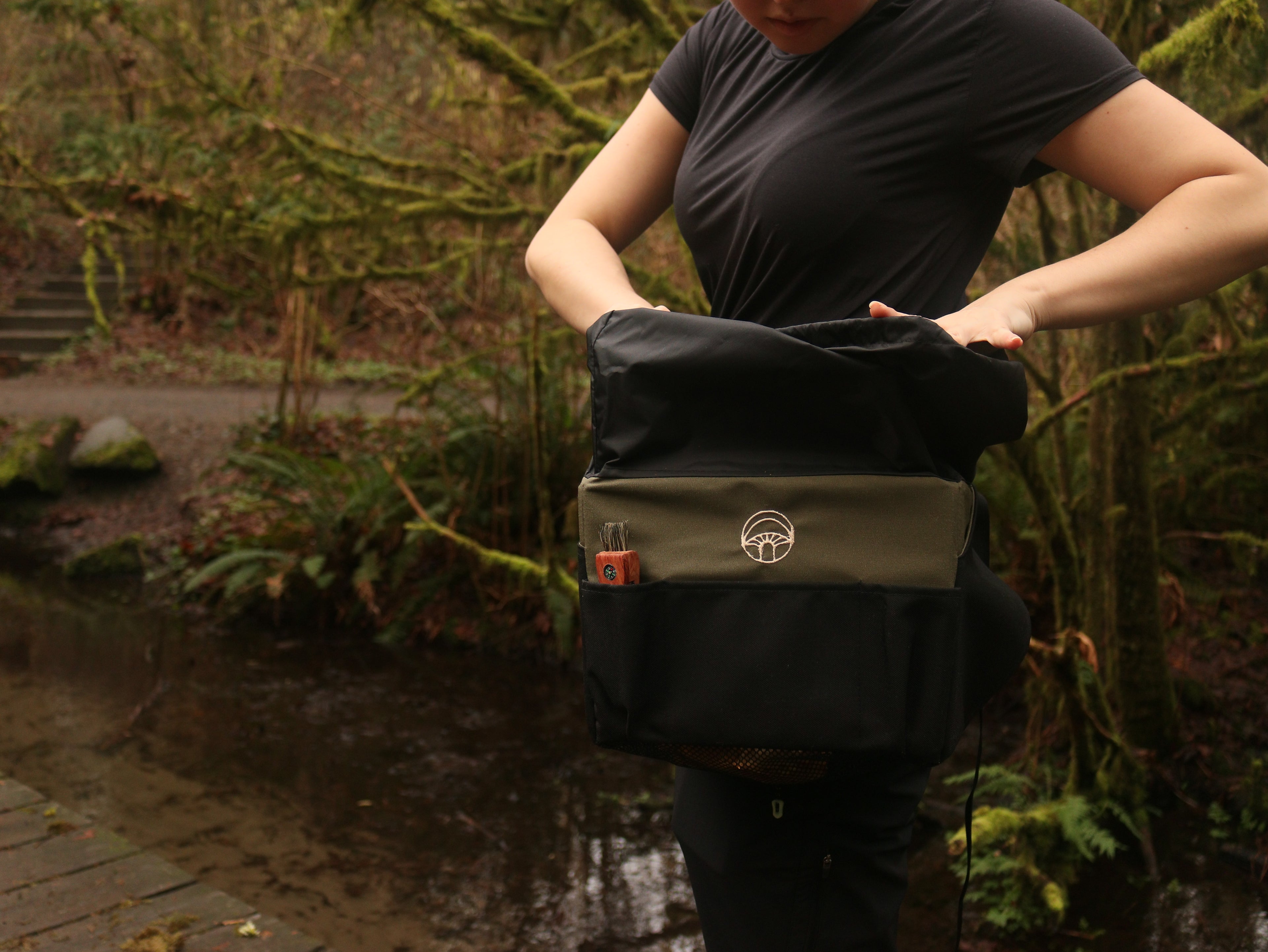 Person holding a black and green bag outdoors with greenery in the background